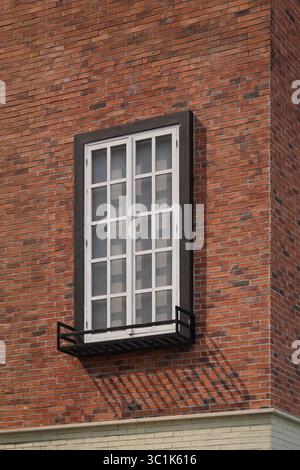A tall classic white window with a black frame set in a red brick wall. Minimalist architectural detail of a building facade with a clean pattern. Stock Photo
