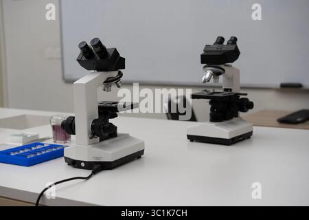 Two modern microscopes on a white table in a science laboratory or classroom. Concept of research, education, biology, and scientific discovery. Stock Photo