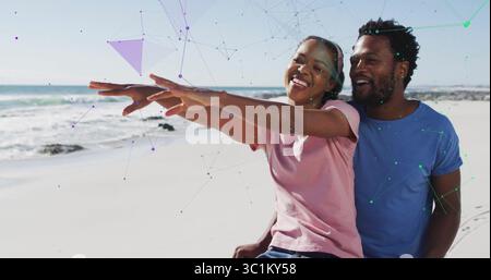 Couple sitting on sandy beach extending arms forward, with pink and light blue t-shirts and jeans Stock Photo