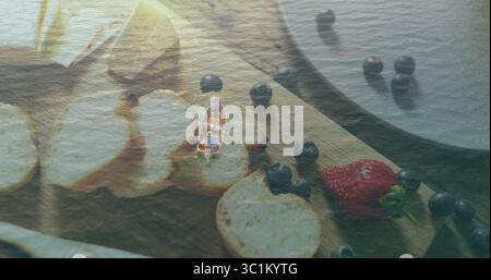 Men in rowboat rowing on calm lake, with cutting board holding bread slices blueberries strawberry Stock Photo