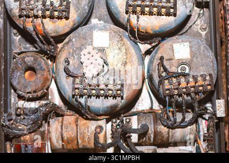 Electrical panel damaged after a fire with charred wires and melted components indicating intense heat exposure. Rusted and blackened surfaces suggest Stock Photo