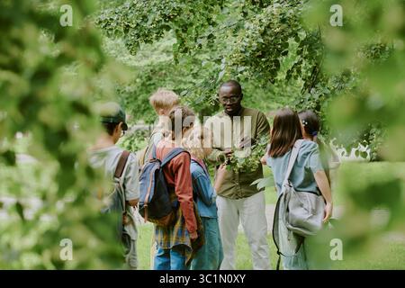 Male Teacher Guiding Diverse Group of Children Exploring Nature in Park Stock Photo
