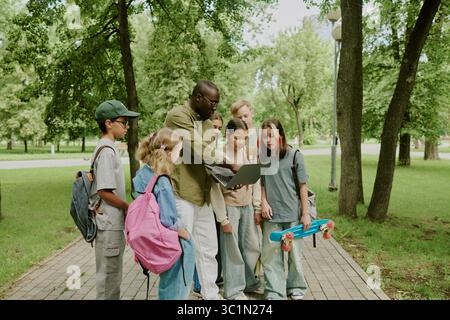 Multiethnic Children Listening to Male Teacher Explaining Lesson in Park Stock Photo
