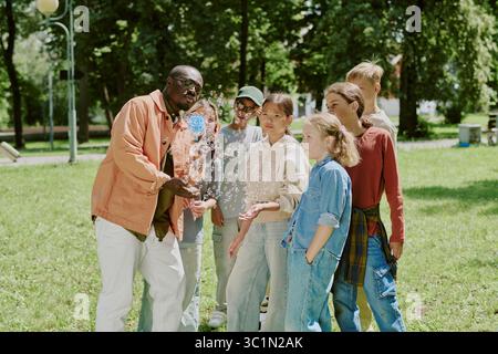 Multiethnic School Teacher Blowing Bubbles with Children Outdoors in Park Stock Photo