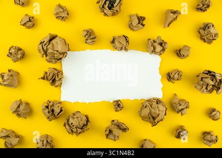 Crumpled Brown Paper Balls with Blank Sheet in Center on Yellow Background for Creative Design and Marketing Stock Photo