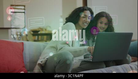 Leaning mother and daughter chatting online on laptop near patterned sofa pillows and wooden table Stock Photo