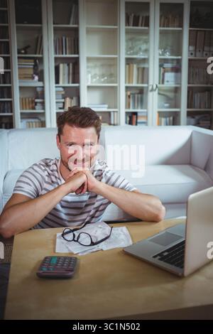 Wooden table is featuring scattered documents, glasses, calculator and open laptop in living room Stock Photo