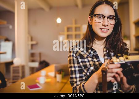Vintage film camera resting on wooden table in warm-lit studio with notebook, pens, coffee mug Stock Photo