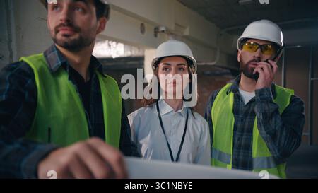 Caucasian men woman workers colleagues discussing talking building plan construction paper project teamwork architects males female civil engineers Stock Photo