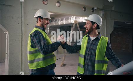 Two happy Caucasian men greeting friends buddies males guys workers in uniform helmets business construction teamwork engineers architects meeting Stock Photo
