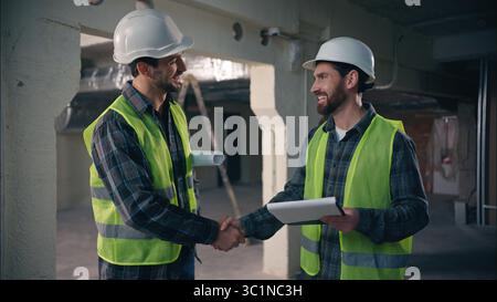 Two glad Caucasian men builders discuss building project in construction architects handymen talking paper draft workmen guys working document Stock Photo