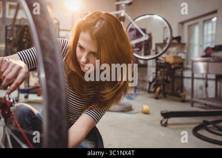 Woman kneeling and adjusting bicycle wheel on repair stand at garage workshop using wrench Stock Photo