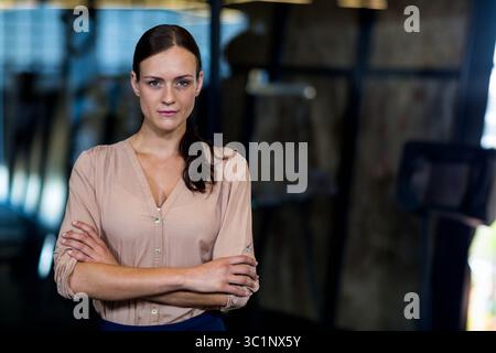 Businesswoman standing with arms crossed in industrial loft, with metal beams and pendant lights Stock Photo
