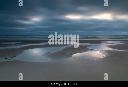 Dark clouds above the beach of Texel during ebb and sunset Stock Photo