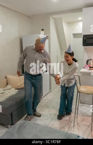 Here's a title following your specifications: Birthday Couple Dancing Home Celebration: Elderly man and woman joyfully dance at home, celebrating a Stock Photo