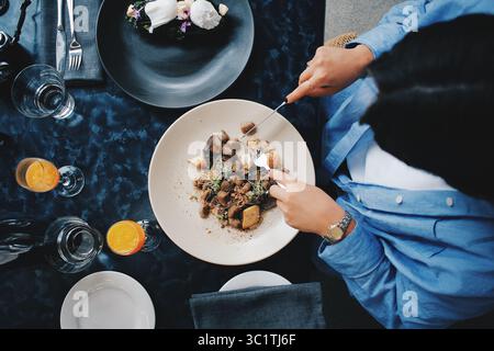 Overhead view of a woman dining at a modern restaurant, eating a gourmet meal with drinks on a dark textured table Stock Photo