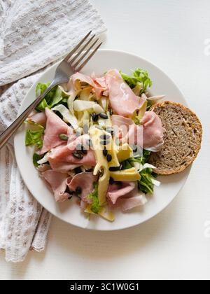 Fresh vegetable salad with prosciutto, cheese, rocket, endive, sunflower seeds and slice of whole grain bread. Healthy food. Directly above. Stock Photo