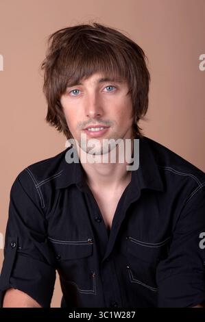 A stylish young man in a black shirt displays a friendly smile in a warm studio. Stock Photo