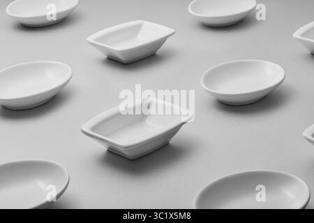 A collection of small, white ceramic dishes arranged on a gray surface. The dishes vary in shape, including oval, square, and rectangular forms. They Stock Photo