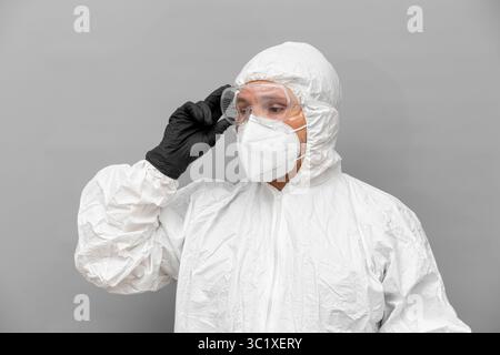 A healthcare professional wearing a full protective suit, gloves, and mask adjusts their headgear while preparing for work in a medical environment du Stock Photo