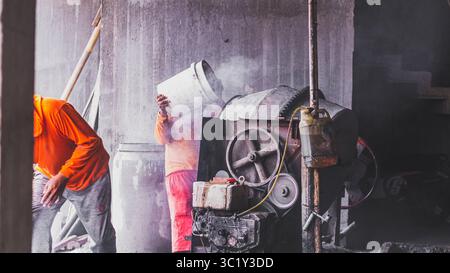 Construction workers collaborate in mixing cement, showcasing solid teamwork and efficiency in real on-site building operations. Stock Photo