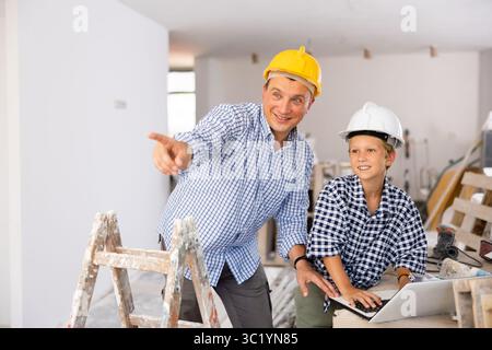 Man architect and boy using laptop while discussing working process in house being renovated Stock Photo