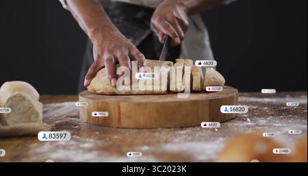 Cutting loaf baker wearing dark apron using knife on cutting board in kitchen, with reaction icons Stock Photo