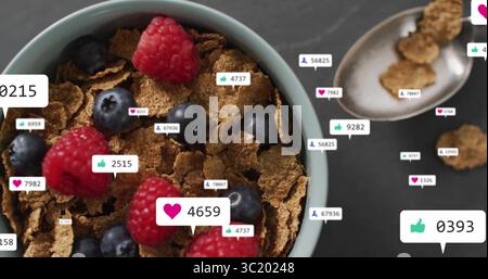 Displaying bowl of bran cereal with raspberries and blueberries in kitchen, floating reaction icons Stock Photo