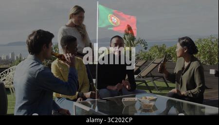 Socializing five friends sitting around coffee table with beers on rooftop terrace, Portuguese flag Stock Photo