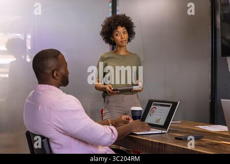 Diverse coworkers collaborating over wooden table with laptop, tablet and coffee in conference room Stock Photo