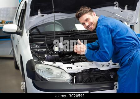 Male mechanic in garage leaning into car engine under open hood showing support rod, copy space Stock Photo