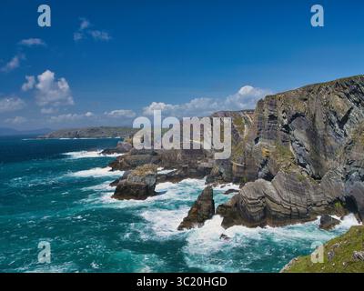 Dramatic cliffs tower over the Atlantic Ocean at Mizen Head, Ireland, under a bright blue sky. Stock Photo