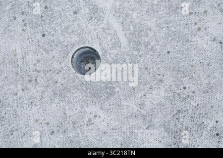 Close-up of an old abandoned mini golf course hole with a weathered concrete surface and metal cup detail. Stock Photo