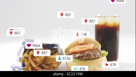 Displaying cheeseburger with lettuce and tomato by fries and cola on table, with notification icons Stock Photo