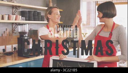 High-fiving two baristas in red aprons behind coffee counter, espresso machine and chalkboard sign Stock Photo