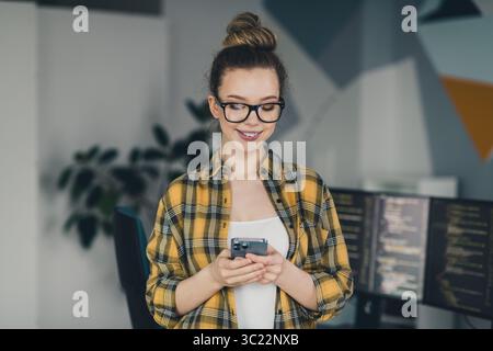 Young professional woman using a phone while coding in a trendy workspace Stock Photo