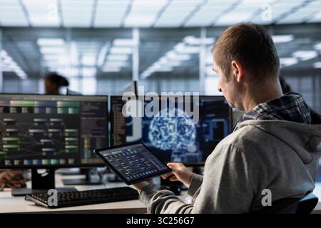 Machine learning professional monitoring server hub with tablet using AI software. Technician overseeing rackmounts in data center using artificial intelligence technology Stock Photo