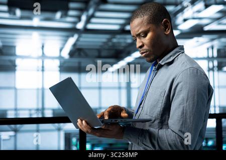 Technician in data center with laptop integrating AI driven automation tools, running predictive maintenance routines, analyzing operational metrics, ensuring continuous uptime, managing data flows Stock Photo