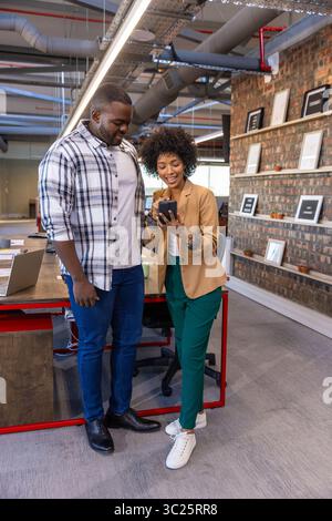 Diverse coworkers standing and reviewing smartphone at wooden desk in office with laptop Stock Photo