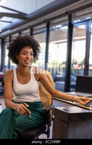 African American woman working on laptop, smiling and using stylus on tablet in coworking office Stock Photo