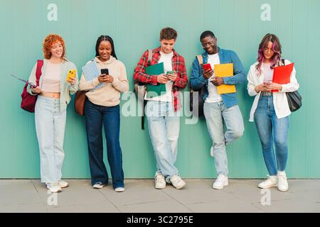 A lively and diverse group of students happily interacting with their smartphones, sharing moments with one another. Each student is focused on their Stock Photo