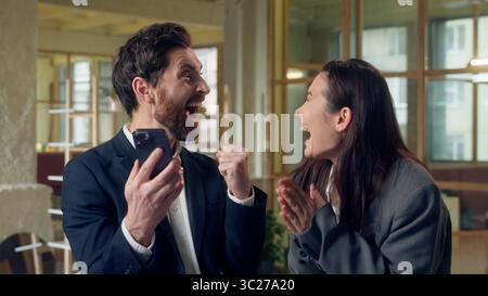 Excited two business woman man celebrating win showing mobile phone green screen chroma key mock up Caucasian Korean businesspeople cheering winner Stock Photo