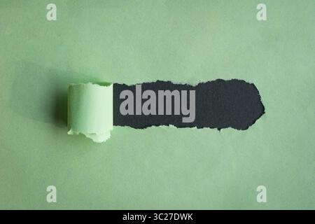 Hole ripped in green paper on black background. Copy space. Stock Photo