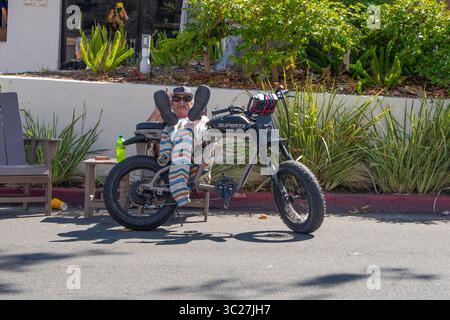 Older male with his feet propped up on his e-bike while resting on State Street in Santa Barbara, California. Stock Photo