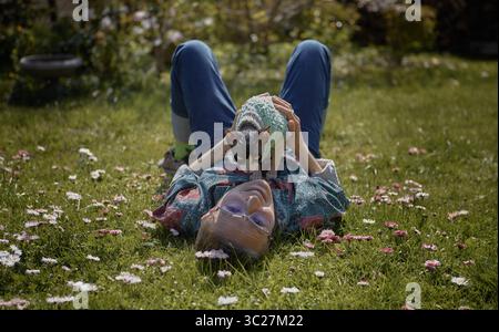 Woman playing with a Sphynx cat while lying in a field of daisies, smiling joyfully. Stock Photo