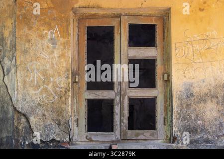 A faded wooden window, set in a cracked, vintage wall, exudes a sense of history and age. The grunge texture adds depth to the weathered facade. Stock Photo