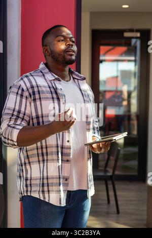 African American man standing in modern office lobby holding tablet and reviewing data on screen Stock Photo