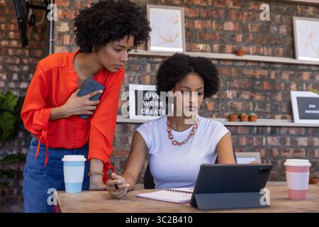 Diverse female coworkers collaborating at creative office desk using smartphone and tablet Stock Photo