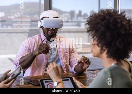 Diverse coworkers collaborating with man wearing VR headset using tablet and phone at office table Stock Photo