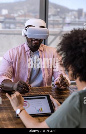 African American coworkers using VR headset and tablet analyzing charts with wristwatch in office Stock Photo